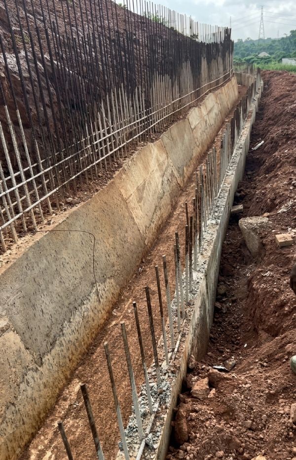 Concrete foundation drainage trench with exposed vertical steel rebar.