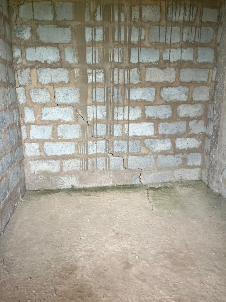 Internal blockwork wall with cracking and moisture staining near floor level.