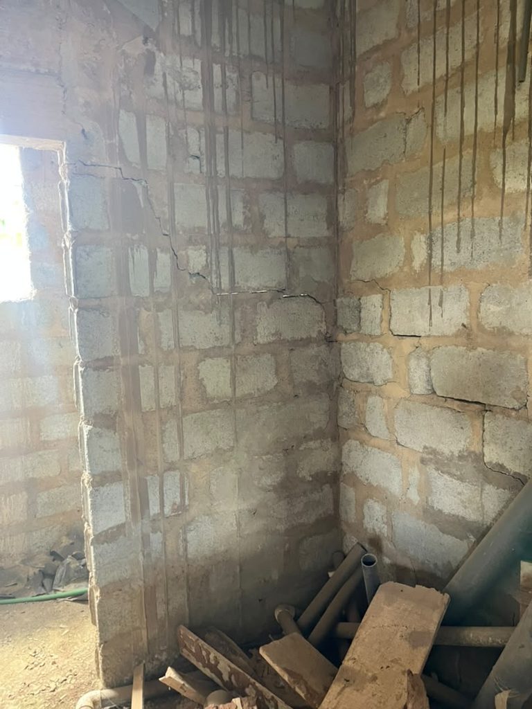 Cracked blockwork beside a doorway with a service channel cut into the wall.